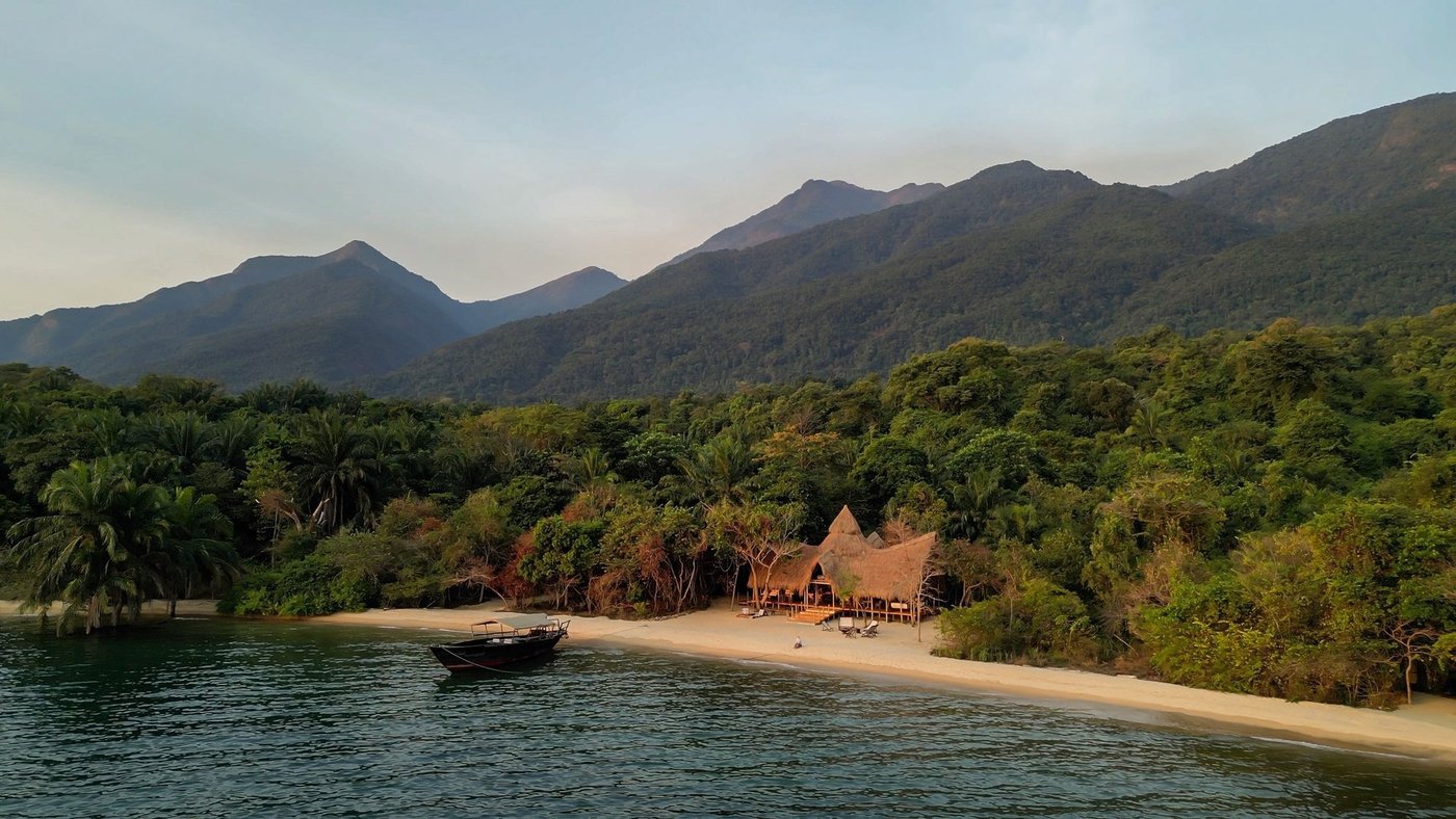 A wooden dhow rests off the beach below Greystoke Mahale's thatched roofline