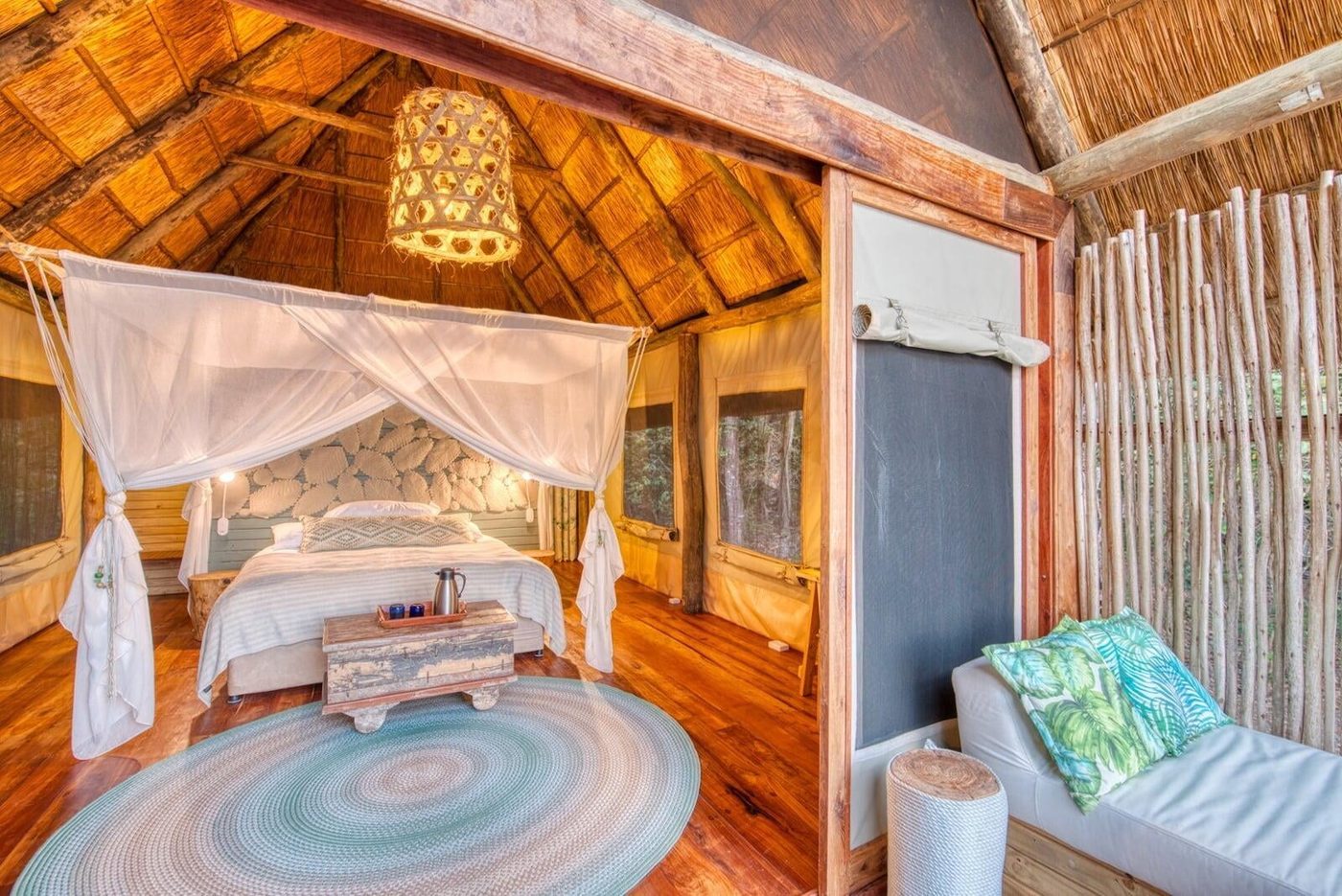 A canopy bed under thatch opens to the forest at Mbali Mbali Mahale Lodge