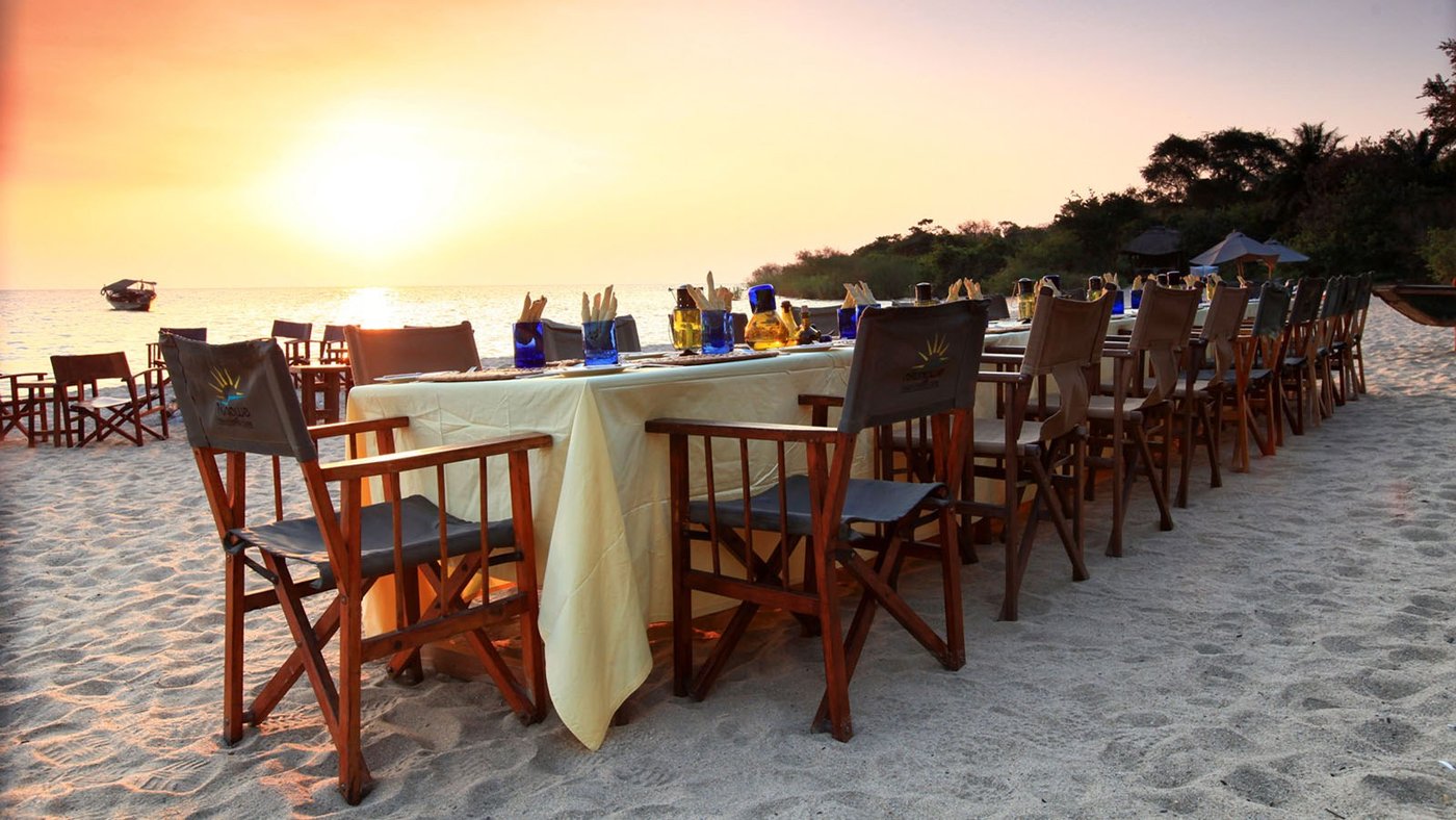A long dining table set on the beach at sunset, Nkungwe Beach Lodge