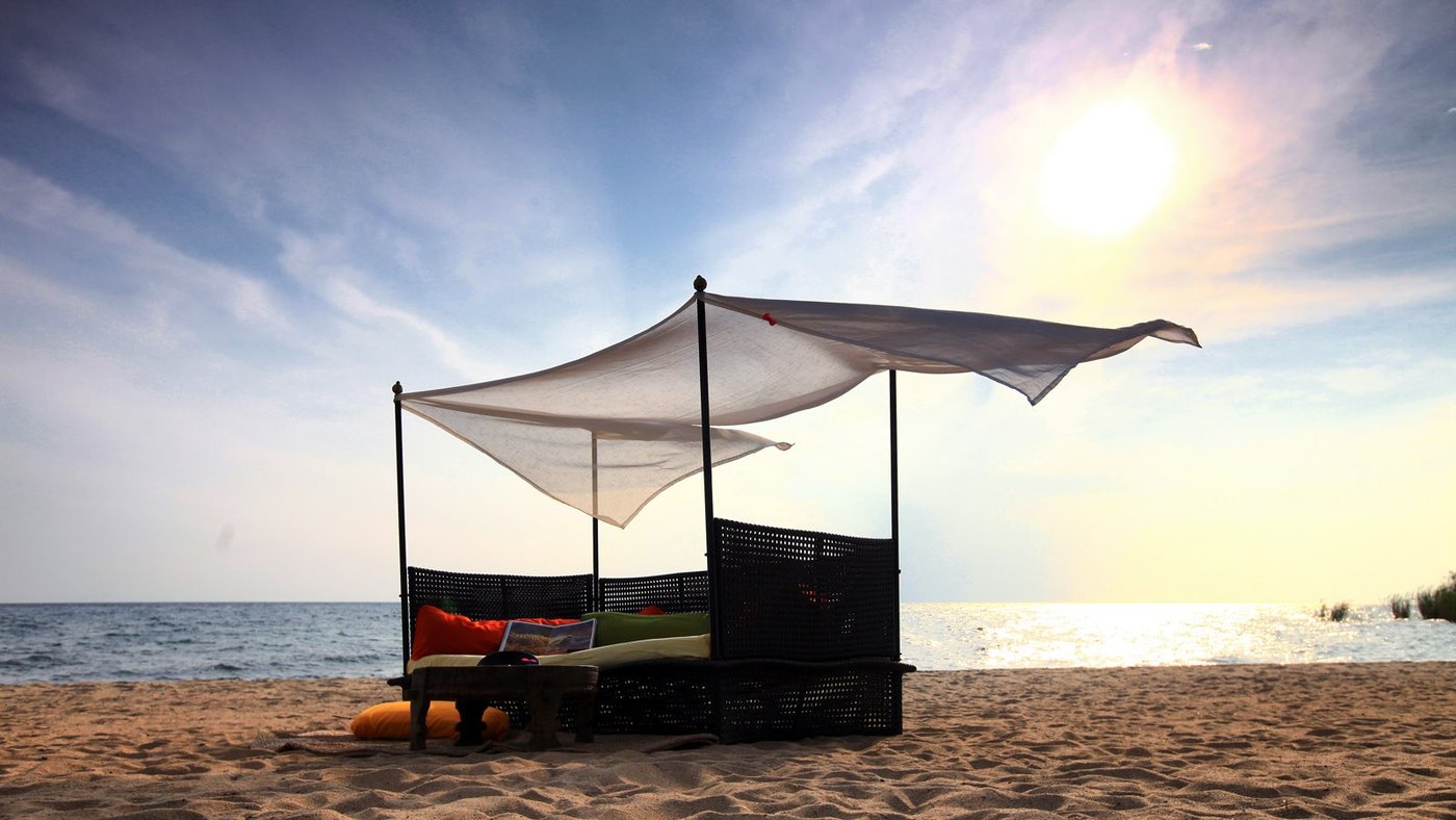 A canopied daybed stands on the beach at Nkungwe Beach Lodge